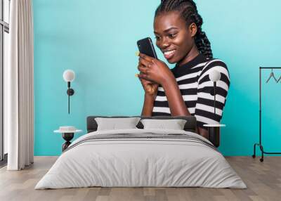 Portrait of american curly woman holding black mobile phone in hands isolated over blue background Wall mural